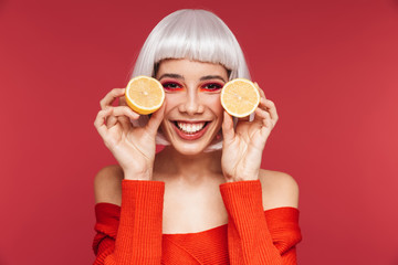 Beautiful young woman isolated over red wall background holding lemon.