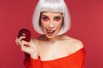 Beautiful young woman isolated over red wall background holding apple.