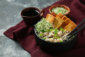 Tasty rice with tofu cheese in bowl on grey table