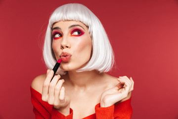 Woman with bright red makeup isolated over red wall background holding lipstick.