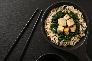 Tasty rice with tofu cheese in bowl on dark table