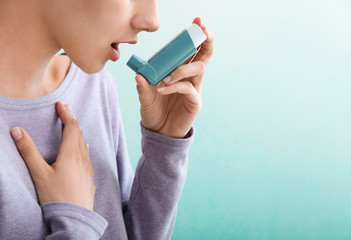 Young woman using inhaler against asthma on color background - obrazy, fototapety, plakaty