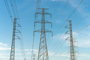 Many high voltage power pole and lines with bright blue sky