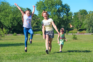 Obraz na płótnie Canvas Happy mother having fun jumping with her daughters on green grass