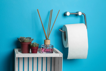 Roll of toilet paper hanging on color wall with reed diffuser in restroom