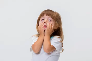 Close-up portrait of little girl's face. Girl grimacing, covering her face with her hands © Yarkovoy