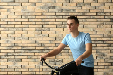 Fototapeta na wymiar Portrait of handsome teenage boy with bicycle near brick wall