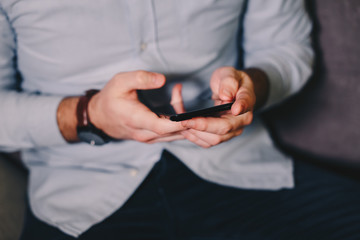 Close up view of male hands using smartphone on the living room couch.