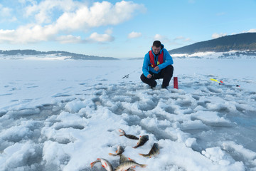 Fisherman catching fish on a frozen lake on the snow. Ice fishing. Horizontal. Selective focus