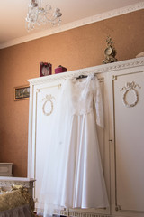 Bridal satin dress hanging on the white closet. White lace dress in a beautiful interior. Morning of the bride preparing for the wedding