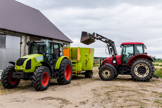 Tractor with front end loader loads the food into a distributor of animal feed for cows. Necessary equipment for a dairy farm.