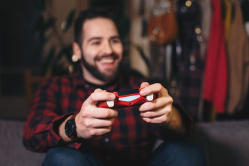 Portrait of a young man playing a video game in his living room, happy because he's winning. Focus on video game controller.