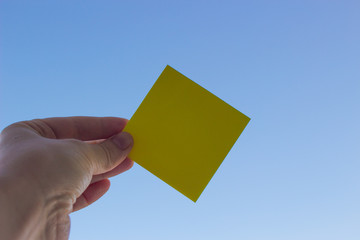 Yellow sticker in hand on blue sky background