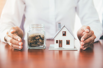 Saving money for house and real estate. Woman hand protecting on stack coins and house model on...