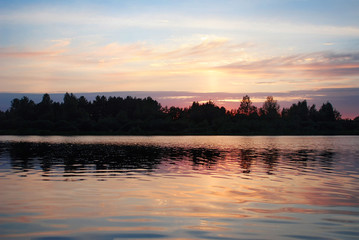 Reflection Of Sky, Clouds And Trees In Lake during sunset in the background