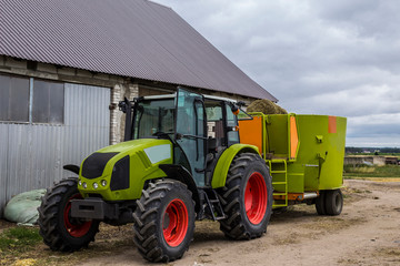 Tractor with a trailer for mixing and distribution of feed for cows. Behind the tractor is a barn...