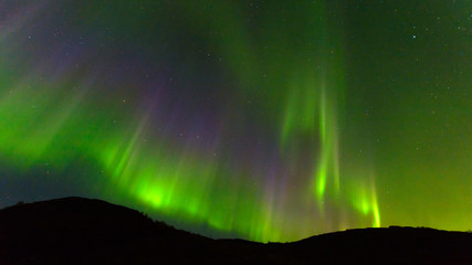 Northern, aurora borealis in the sky above the hills. Violet and green. Color.