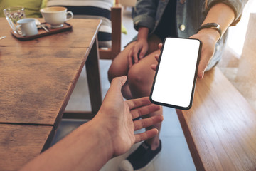Mockup image of a woman holding and showing white mobile phone with blank black desktop screen to...