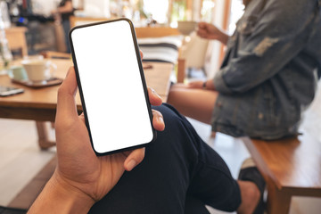 Mockup image of a man's hand holding black mobile phone with blank white screen with woman sitting in cafe