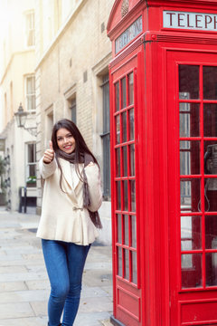 Attraktive, junge Frau auf Reisen in London zeigt den Daumen hoch vor einer klassich, roten Telefonzelle