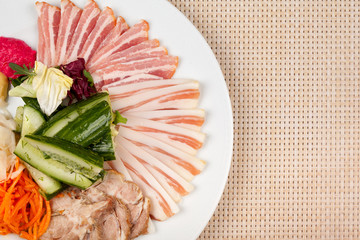 Meat and lard with vegetables on a white plate on the table.