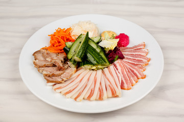 Meat and lard with vegetables on a white plate on the table.