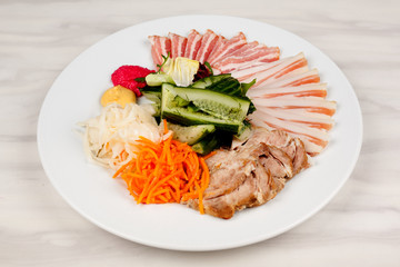 Meat and lard with vegetables on a white plate on the table.
