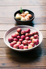 Closeup of bowls of fresh red apples and onions sprinkled raindrops on wooden table
