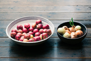 Closeup of bowls of fresh red apples and onions sprinkled raindrops on wooden table