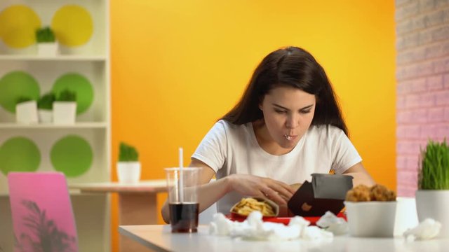 Young lady feeling nausea while tasting fast food burger, unhealthy nutrition