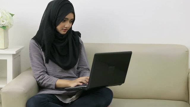 Attractive young woman in head scraf using laptop while sitting on couch