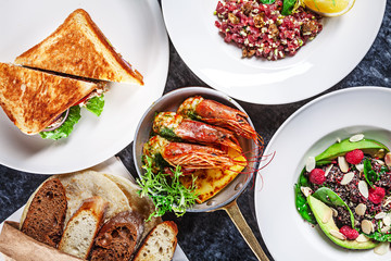 Top view on food party table. Pan of shrimps, beef tartare, sandwich and salad with avocado on marble stone. Restaurant food menu, recipe photo on marble table