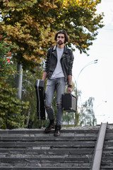Street musician holding a case with a guitar and amplifier. Goes down the stairs to the underground passage. Vagrant lifestyle. Playing to make money a living. Unemployed musician. Future rock star.