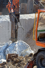 Fototapeta premium Demolition excavator with hydraulic hammer resting between two pieces of just divided concrete block