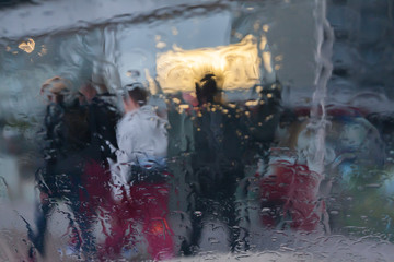 Rain drops on car glass, focus on raindrops. View to the street and people.