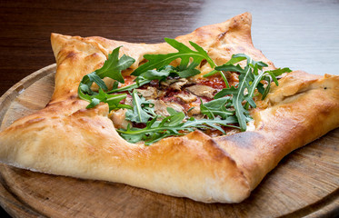 Star-shaped pizza with ham and arugula on a wooden board.
