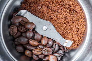 A metal electric coffee grinder. One side of coffee grinder with whole grains of coffee, another with ground. Closeup, selective focus, top view