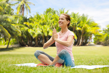 fitness, yoga and healthy lifestyle concept - happy woman meditating in exotic summer park over french polynesia background