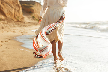 Portrait of caucasian girl 20s walking with waving scarf, along seashore