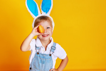 funny happy child boy with easter eggs and bunny ears on yellow.