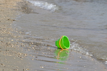 Green toy bucket lies on the beach