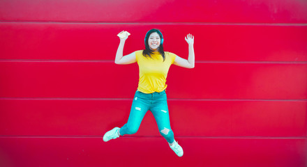 Fototapeta na wymiar Asian millennial girl jumping and listening music outdoor