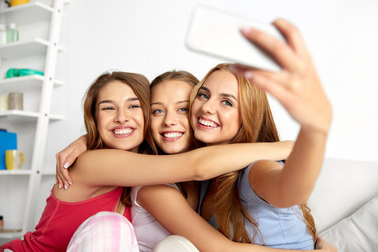 friendship, pajama party and technology concept - happy friends or teenage girls taking selfie by smartphone at home