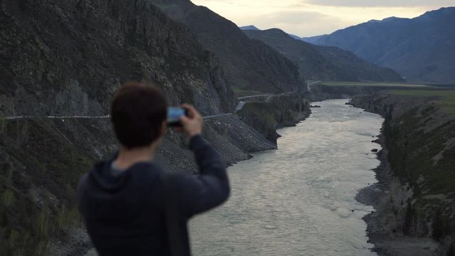 Hiker with mobile device or smartphone shooting photography of mountain river. Young male traveller using cellphone to take pictures of beautiful nature scenery.