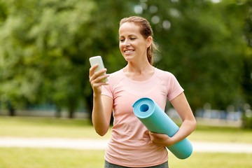 fitness, sport and healthy lifestyle concept - happy smiling woman with exercise mat and smartphone at summer park