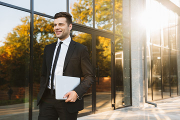 Young businessman walking outdoors at the street with laptop computer.