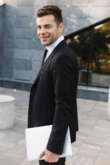 Young businessman walking outdoors at the street with laptop computer.