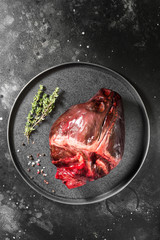 Raw reindeer heart on black plate on dark background
