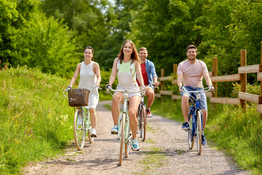 people, leisure and lifestyle concept - happy young friends riding fixed gear bicycles on country road in summer