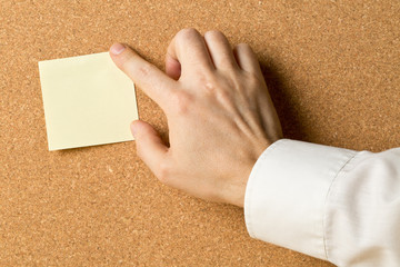 Business man pinning empty yellow sticky paper memo note on cork board